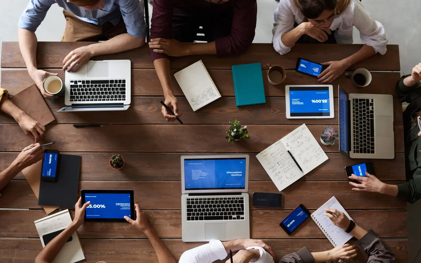Equipe reunida em volta de uma mesa de madeira com notebooks, tablets e cadernos